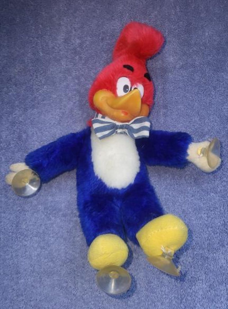 May include: A plush toy of Woody Woodpecker, featuring a red head, yellow beak, and blue body. The toy has a white chest, a striped bow tie, and yellow feet. It holds cymbals in each hand, and is a vintage collectible.