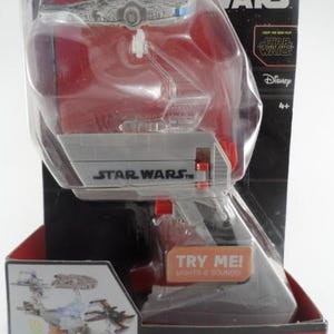 May include: A Star Wars Flight Controller toy in its original packaging. The package features the Star Wars logo, the Disney logo, and the Hot Wheels logo. The toy is a handheld accessory that includes lights and sounds. The package also says "Flies up to 3 starships!"