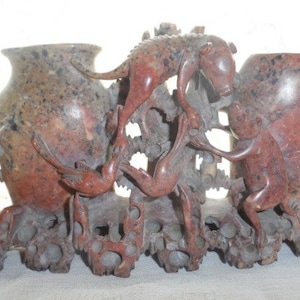 May include: A red and brown stone sculpture of two vases with a bird and a dog on top. The sculpture is carved with intricate details and has a rustic look.