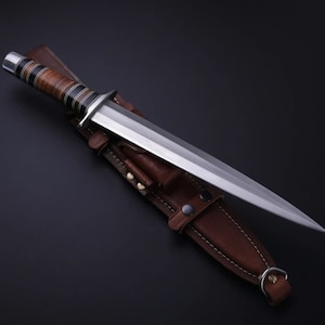 May include: A silver dagger with a brown leather handle and a brown leather sheath. The dagger has a long, sharp blade and a pointed tip.