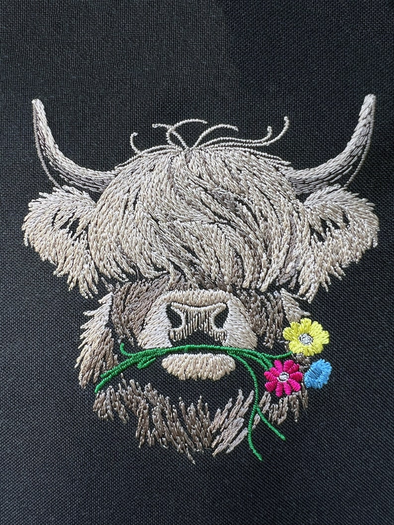 May include: Embroidered design of a Highland cow with brown fur, a white face, and a green stem with pink, yellow, and blue flowers in its mouth.
