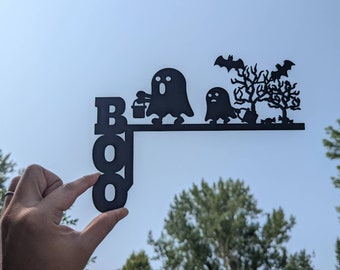Puede incluir: Silueta de metal negro de la palabra "BOO" con dos fantasmas y un árbol con murciélagos. Los fantasmas llevan cubos y caminan hacia el árbol.