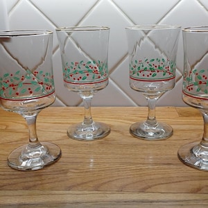May include: Set of four clear glass wine glasses with gold rims. Each glass has a green and red holly design.