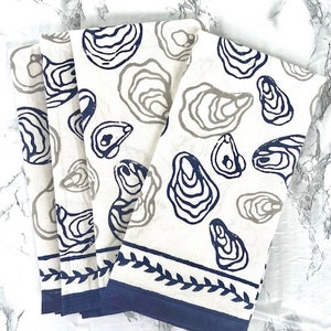 以下が含まれることがあります： 青とグレーのオイスター柄がプリントされた白いコットン製のキッチンタオル3枚セット。タオルは葉の模様の青い縁取りがされています。