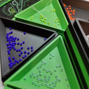May include: Green, black, and white triangular trays with small round beads in each. The trays are used for organizing beads for diamond painting.