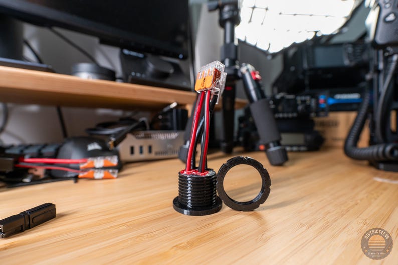 May include: A black electrical component with red and black wires extending from it. A black circular ring sits next to the component. The items are on a wooden surface. The image is well-lit and in focus.