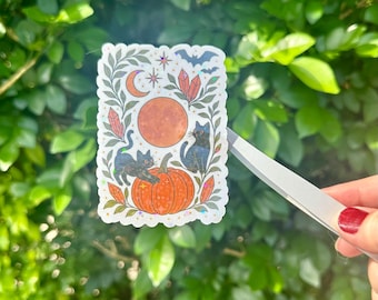 May include: A rectangular sticker featuring a Halloween theme. The sticker has a white border and depicts two black cats, a large orange pumpkin, a full orange moon, and a bat. The background includes leaves, crystals, and a crescent moon.