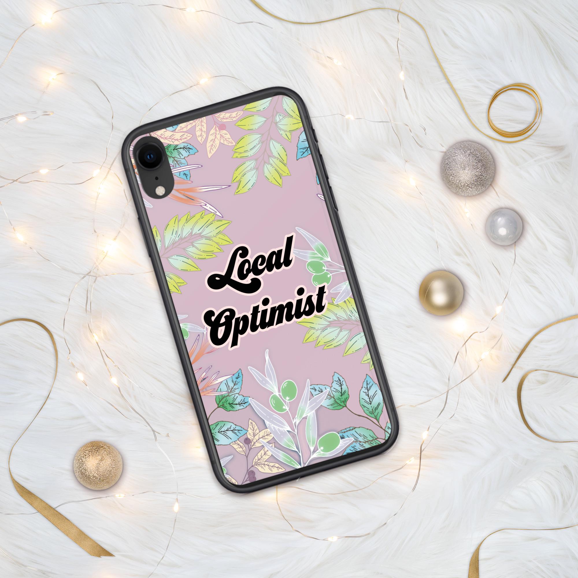 Op de afbeelding: Een zwarte telefoonhoes met een roze achtergrond en een bloemenpatroon. De tekst "Local Optimist" staat in een retro-lettertype op de hoes.