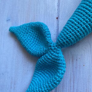 May include: A teal blue crocheted mermaid tail with a pointed fin.