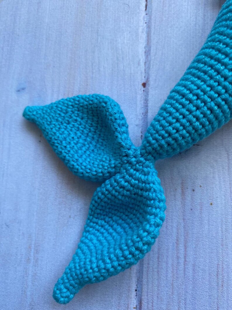 May include: A teal blue crocheted mermaid tail with a pointed fin.