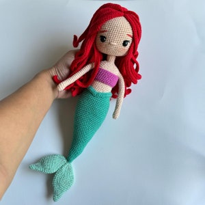 May include: A crocheted mermaid doll with red hair, a pink top, and a green tail.