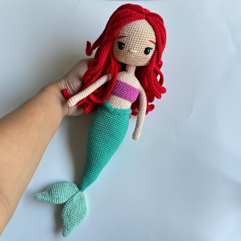May include: A crocheted mermaid doll with red hair, a pink top, and a green tail.
