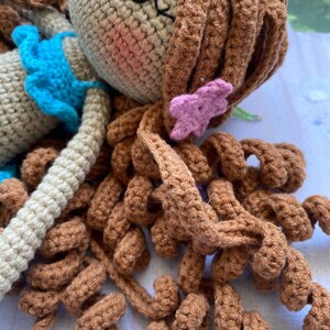 May include: A crocheted doll with brown hair, a blue top, and a pink flower in her hair.