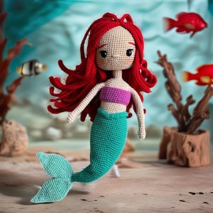 May include: A crocheted mermaid doll with long red hair, a purple top, and a teal tail. The doll is posed with its tail extended and its arms outstretched.