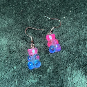 May include: A pair of silver dangle earrings with pink and blue gummy bear charms.