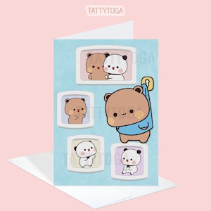 May include: A blue card with a light blue background featuring five cartoon images of a brown bear and a panda bear in different poses. The images are framed in white squares with rounded corners. The text "TATTYTOGA" is at the top of the card.