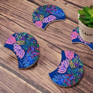 May include: Set of four blue and white ceramic coasters with a floral design. The coasters are shaped like a crescent moon and feature pink, blue, and green flowers.