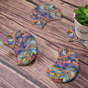 Könnte beinhalten: Vier farbenfrohe, halbmondförmige Untersetzer mit einem wirbelnden, abstrakten Design. Die Untersetzer sind aus Keramik und haben eine glänzende Oberfläche.