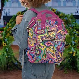 May include: A pink and multi-colored backpack with a swirling abstract pattern. The backpack has a zippered pocket on the front and the text "COLORTHOLOGY" printed on the front.