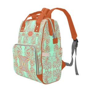 May include: A mint green backpack with a floral pattern in coral and brown. The backpack has brown straps, handles, and trim. It features a front pocket, side pockets, and a zipper closure. The shoulder straps are gray.
