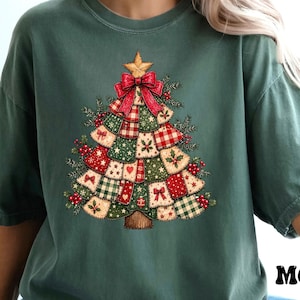 May include: A moss green short-sleeve t-shirt featuring a graphic of a Christmas tree made of various patchwork fabric squares in red, white, and green patterns, topped with a gold star and a large red bow, with the word MOSS printed below.