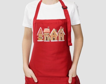 May include: Red apron with a large pocket and adjustable neck strap. The apron features a festive design of gingerbread houses with white icing and candy decorations.