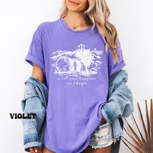 May include: Purple t-shirt with a white graphic of a person walking through a stone archway with a cross above. The text "a lot can happen in 3 days" is below the graphic.