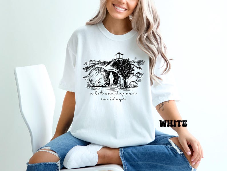 May include: White t-shirt with a black and white illustration of a person walking towards a tomb with a cross above it. The text "a lot can happen in 3 days" is printed below the illustration.