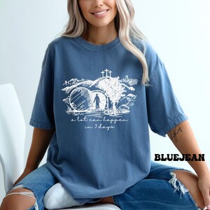 May include: A blue t-shirt with a white graphic of a person walking through a stone archway with a cross above. The text "a lot can happen in 3 days" is below the graphic.