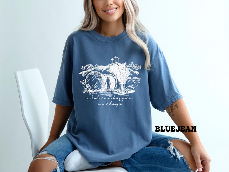 May include: A blue t-shirt with a white graphic of a person walking through a stone archway with a cross above. The text "a lot can happen in 3 days" is below the graphic.