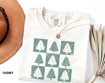 May include: Ivory t-shirt with a green and white Christmas tree design. The design is a checkered pattern of nine trees. The shirt has a tag that says "COMFORT COLORS" and "S - P - CN".