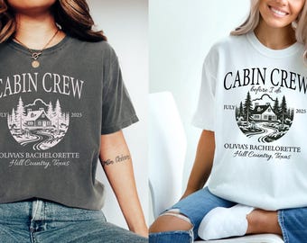 May include: A pepper gray and a white t-shirt, each featuring a graphic of a cabin in the woods with the text CABIN CREW, before I do, JULY 2025, OLIVIA'S BACHELORETTE, and Hill Country, Texas. The shirts have short sleeves and a crew neckline.