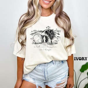 May include: A white t-shirt with a black and white illustration of a tomb, a figure walking away from it, and the text "a lot can happen in 3 days".
