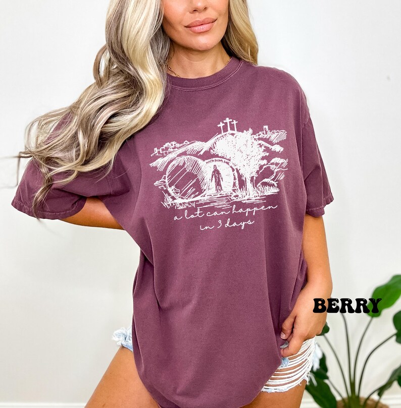 May include: A maroon t-shirt with a white graphic of a person walking through a stone archway with a cross on top. The text "a lot can happen in 3 days" is below the graphic.