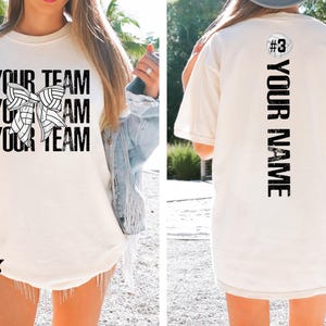 May include: Ivory white t-shirt with the text "Your Team" and a volleyball with a bow on it. The back of the shirt has the text "#3 Your Name" printed vertically.