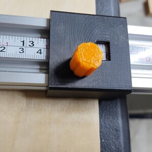 May include: A black and silver ruler with a bright orange knob. The ruler has markings in inches and the knob has a hexagonal shape.