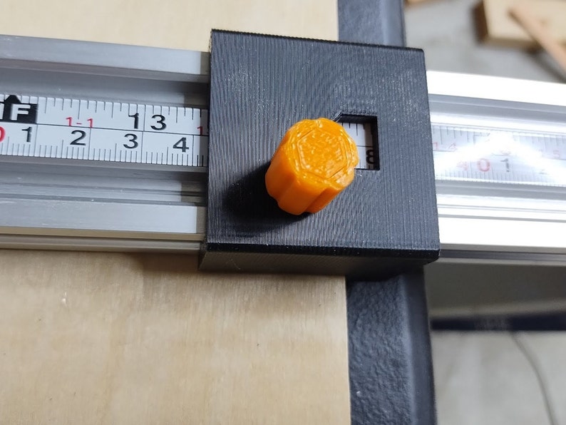 May include: A black and silver ruler with a bright orange knob. The ruler has markings in inches and the knob has a hexagonal shape.