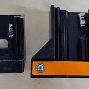 May include: Two black 3D printed parts with a small orange piece in between. The orange piece has two silver screws on either side.