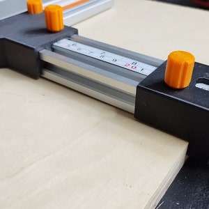 May include: A black and silver woodworking tool with orange knobs. The tool has a ruler with markings from 5 to 20.