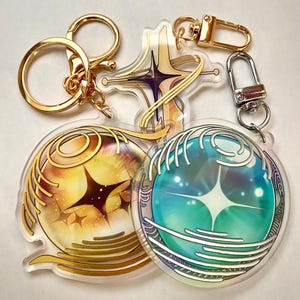 May include: Clear acrylic keychains with gold-colored hardware. One keychain features a starburst design in yellow and orange, another in blue and green. A third keychain has a cross-like design with purple accents.