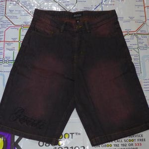 May include: Dark brown denim shorts with a faded red wash and a small embroidered logo that says "Gwest".