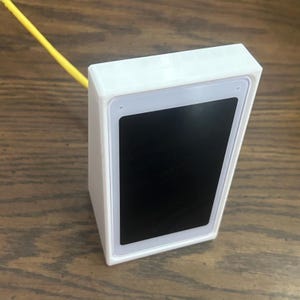 May include: A white rectangular device with a black screen. The device has a light gray border around the screen and a white frame. A yellow cable extends from the top of the device.