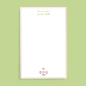 May include: White notepad with a pink border. The top of the notepad has the text "from the desk of Elizabeth Miller" in green text. The bottom of the notepad has a small pink flower illustration.
