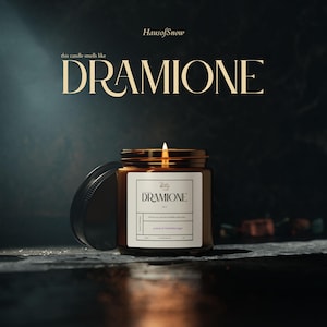 Puede incluir: Una vela encendida en un tarro de cristal marrón con tapa dorada. La etiqueta dice "DRAMIONE" y "potion & forbidden pages". También se ve el texto "this candle smells like" y "HausofSnow". La vela está sobre una superficie oscura.