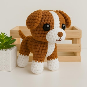 Peut inclure: Un jouet en crochet en forme de chien brun et blanc avec des yeux noirs. Le chien est debout sur une surface blanche.