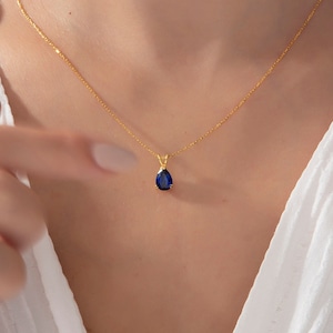 May include: A gold chain necklace with a teardrop-shaped pendant featuring a dark blue gemstone.