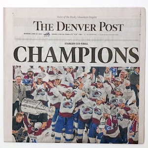 May include: A newspaper headline announcing the Denver Avalanche as Stanley Cup Champions. The image shows the team celebrating with the Stanley Cup trophy.