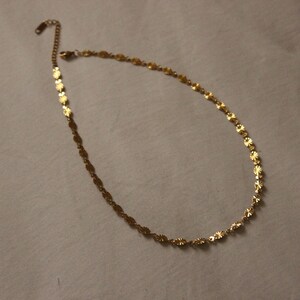 Puede incluir: Un delicado collar dorado con un dise&ntilde;o floral. El collar presenta peque&ntilde;os dijes en forma de flor unidos para formar una cadena. El collar se muestra sobre un fondo neutro. Mide aproximadamente 40 cm.