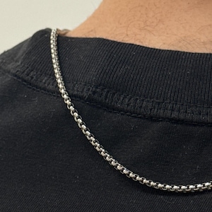 Pode incluir: Um colar de corrente prateada com um design arredondado e texturizado. O colar é exibido contra um fundo preto, criando um contraste que destaca os detalhes da joia. A corrente é provavelmente feita de metal.