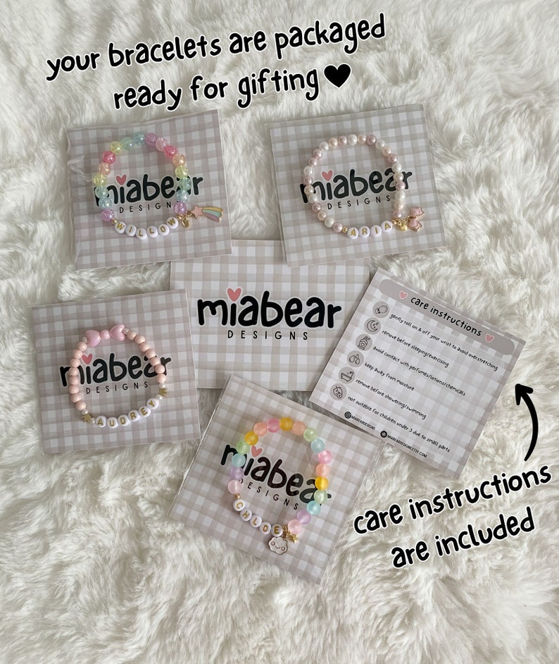 Pode incluir: Quatro pulseiras de contas coloridas com nomes personalizados em cart&otilde;es brancos. Cada pulseira tem um amuleto. Os cart&otilde;es t&ecirc;m um padr&atilde;o xadrez rosa e branco. Tamb&eacute;m est&aacute; inclu&iacute;do um cart&atilde;o com instru&ccedil;&otilde;es de cuidados.